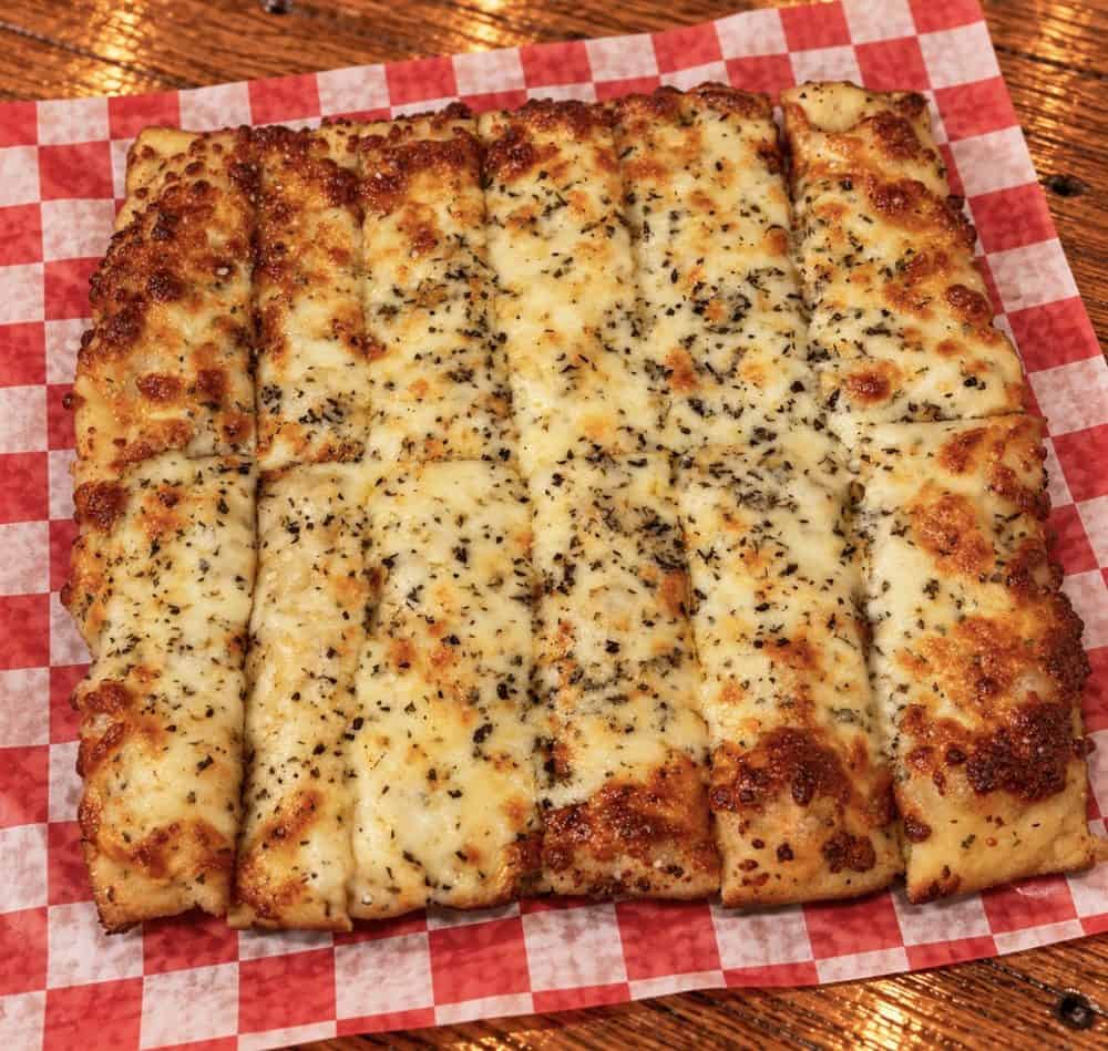 lipw-cheesy-breadsticks-web Breadsticks topped with golden melted cheese and herbs on red-and-white checkered paper.