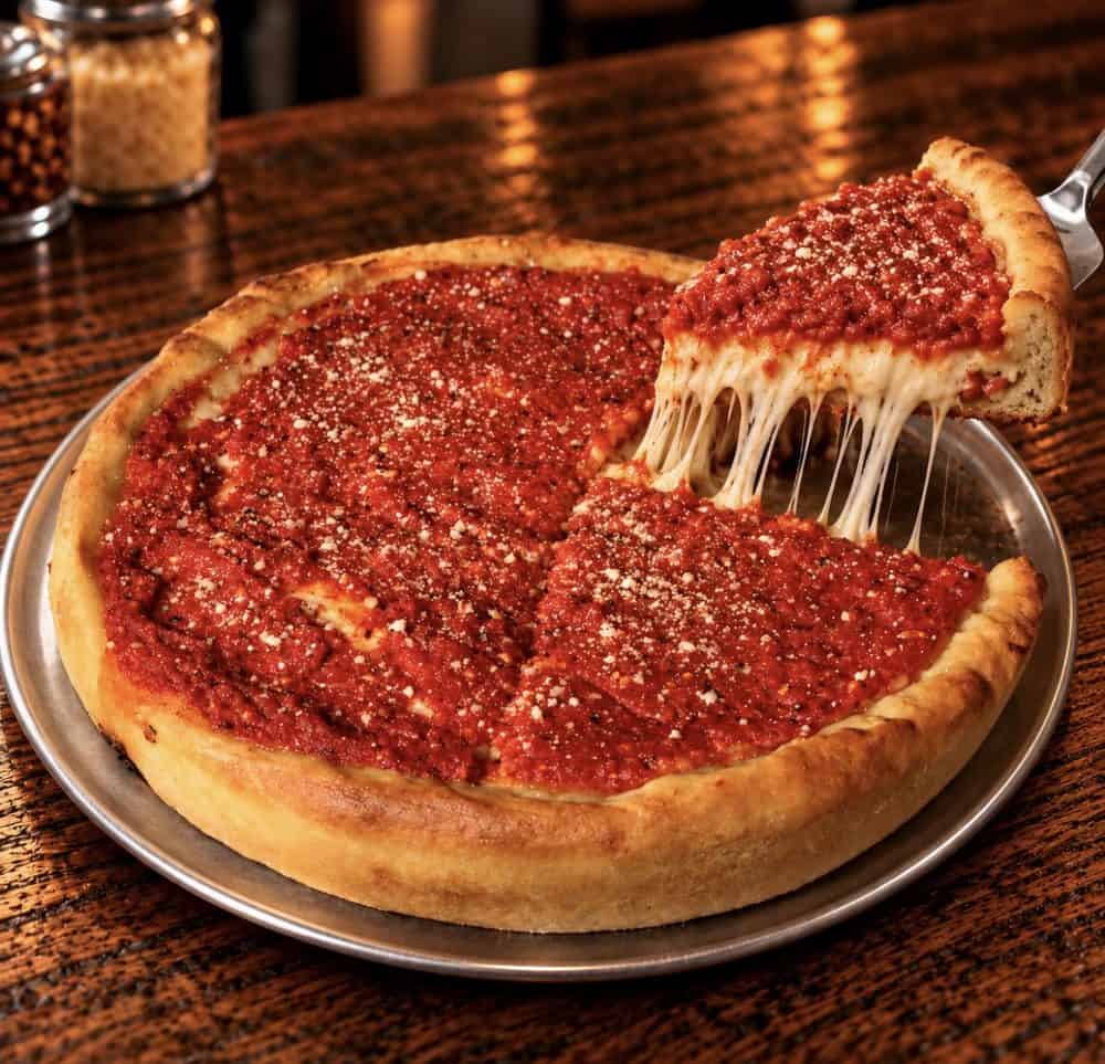 lipw-chicago-style-stuffed-pizza-web Chicago-style stuffed pizza topped with tomato sauce and grated cheese, with a slice lifted to reveal stretchy melted cheese.