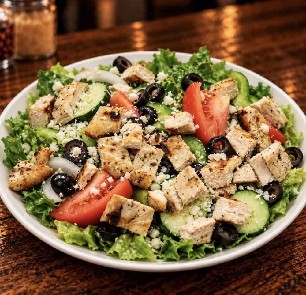 Grilled chicken salad with lettuce, tomatoes, cucumbers, black olives, onions, and crumbled cheese.