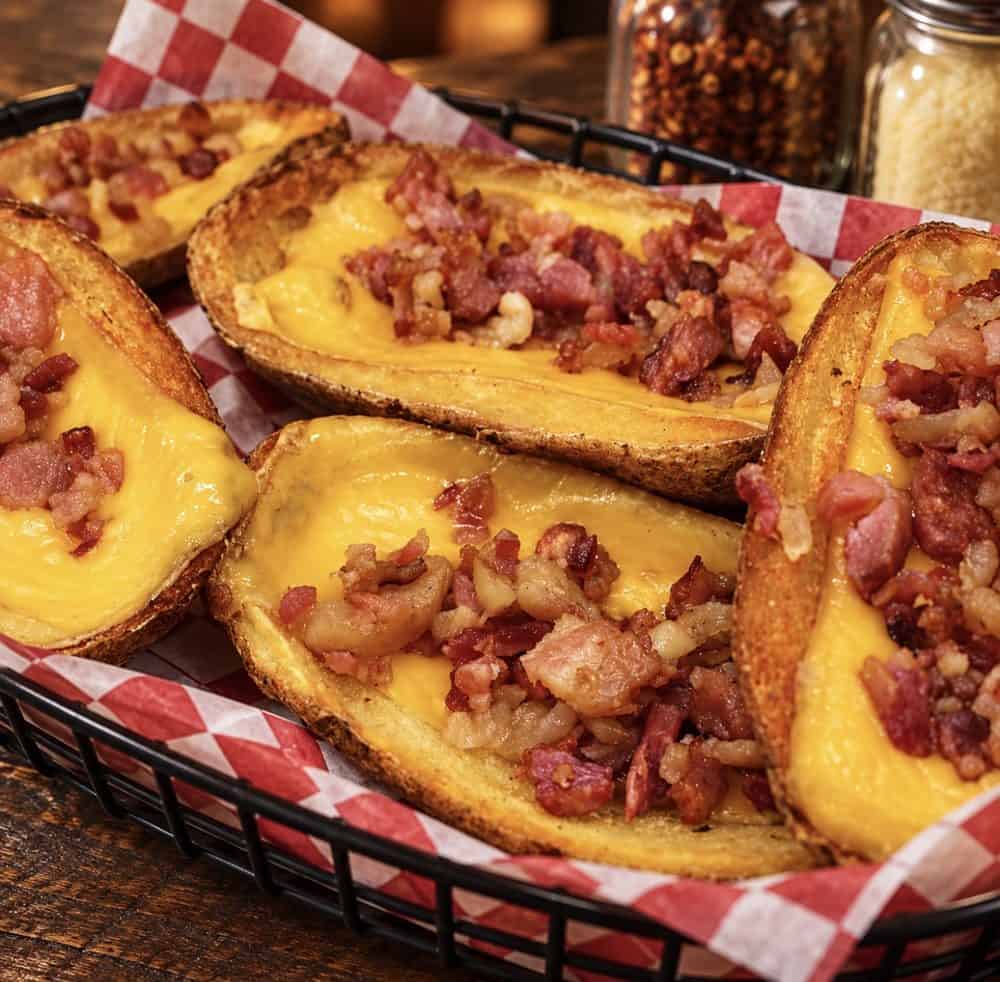 Crispy potato skins filled with melted cheddar cheese and chopped bacon in a checkered-paper-lined basket.