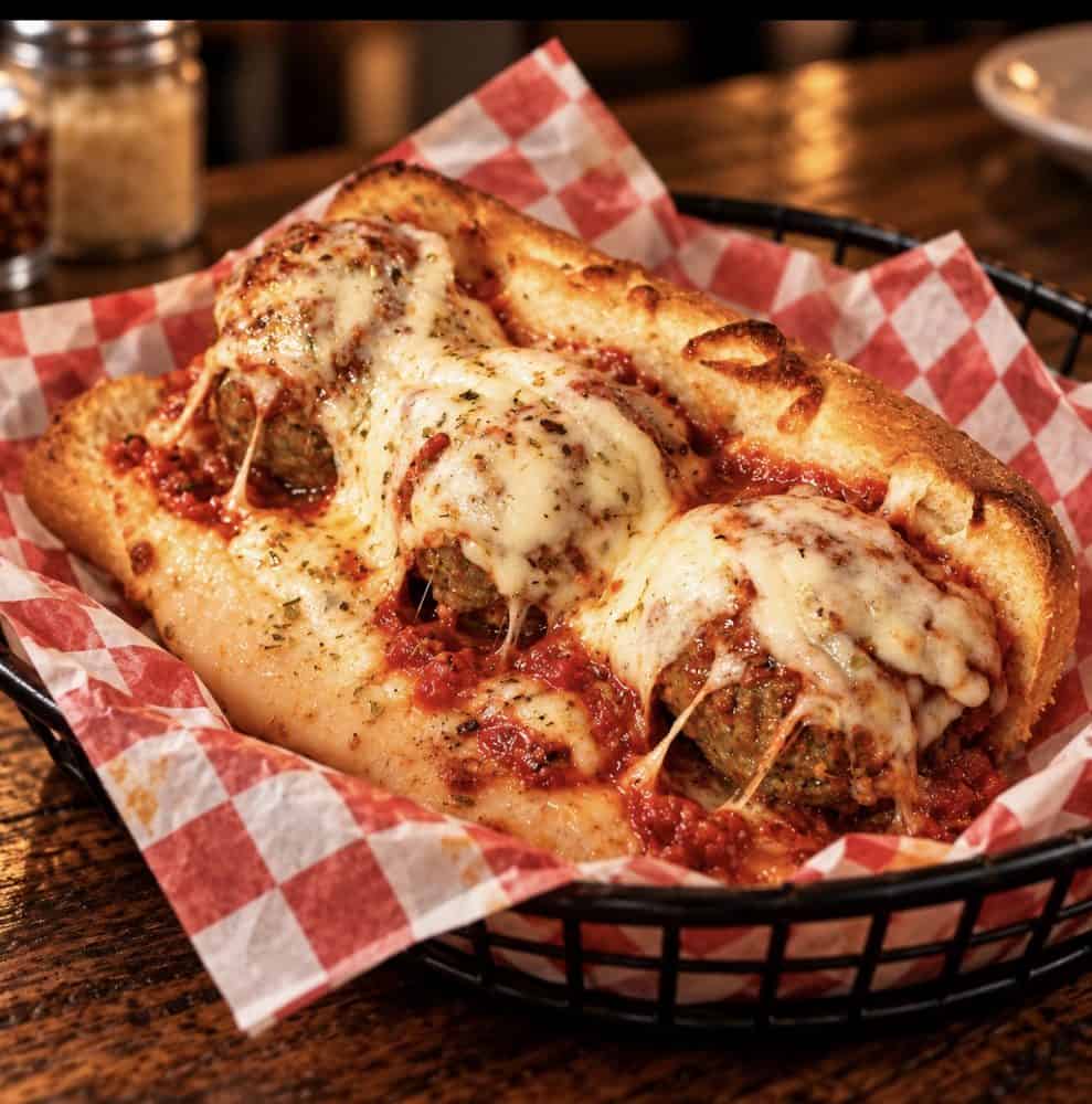 Three meatballs topped with tomato sauce, melted cheese, and herbs in a toasted sandwich roll.