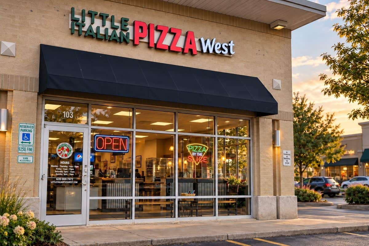 lipw-storefront-dark-awning-wordpress Little Italian Pizza West storefront with a dark awning, illuminated signage, and warm evening light.
